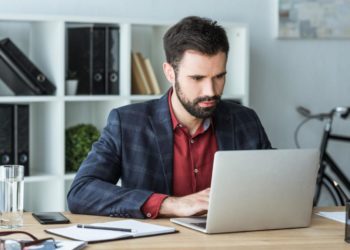 Junger Mann sitzt vor dem Laptop am Schreibtisch, Bewerbung schreiben, künstliche Intelligenz bei Bewerbungen